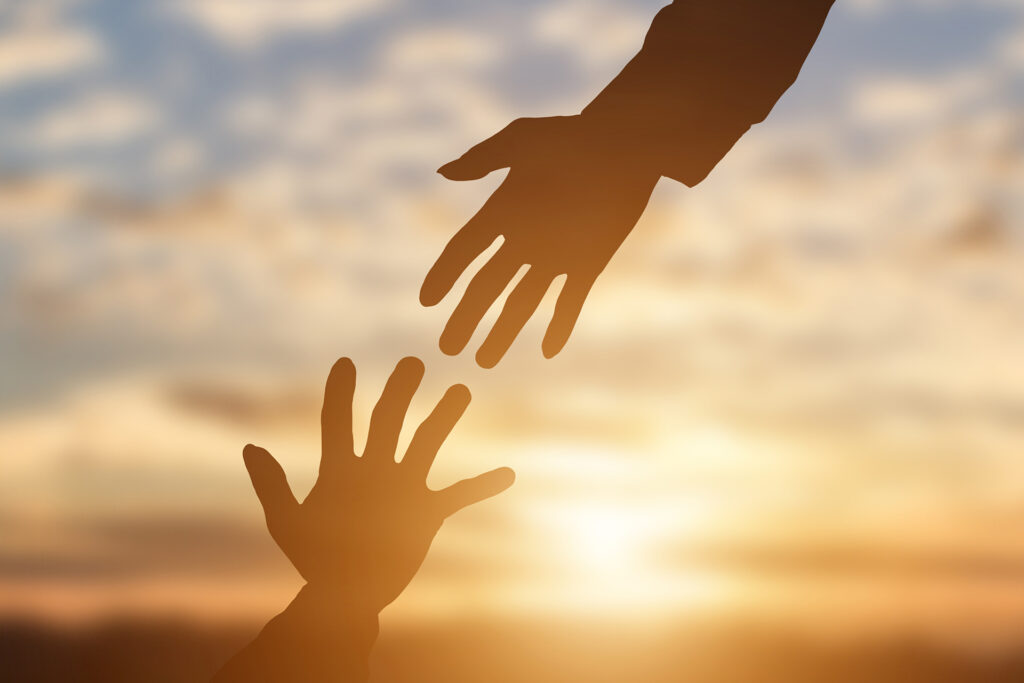 Deux mains tendues l'une vers l'autre au coucher du soleil, symbole d'entraide